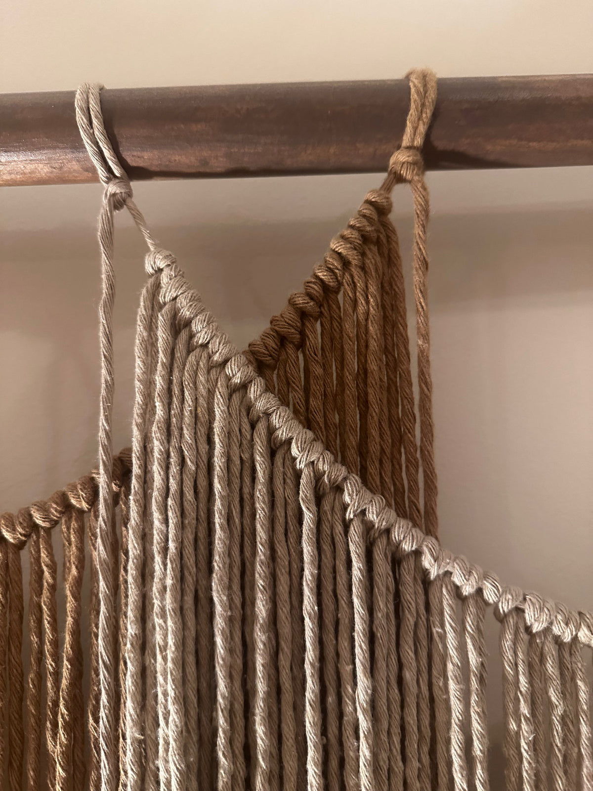 Close-up van Suspenso Terra van Nyra Atelier: gedraaide koorden geknoopt langs de gedrapeerde bovenrand van een macramépaneel, hangend aan een houten tak