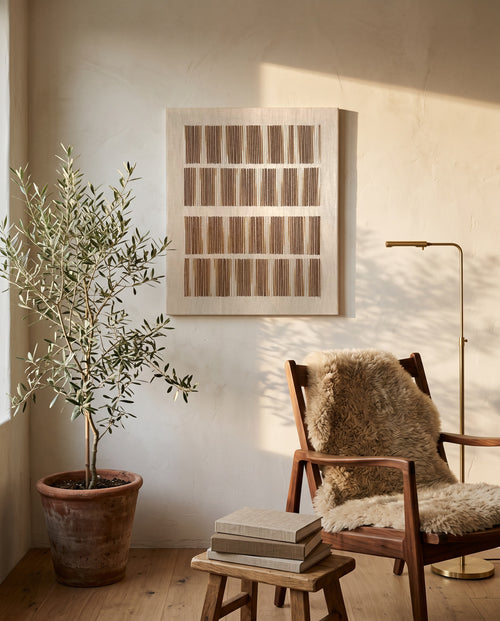 Andante, handmade wool wall art by Nyra Atelier, hung vertically in a sunlit reading corner with an olive tree, a wooden chair with a sheepskin and a stack of books. AI-assisted lifestyle image: the setting is illustrative and the canvas is our real product photo; please refer to our real product photographs for the actual item’s details.