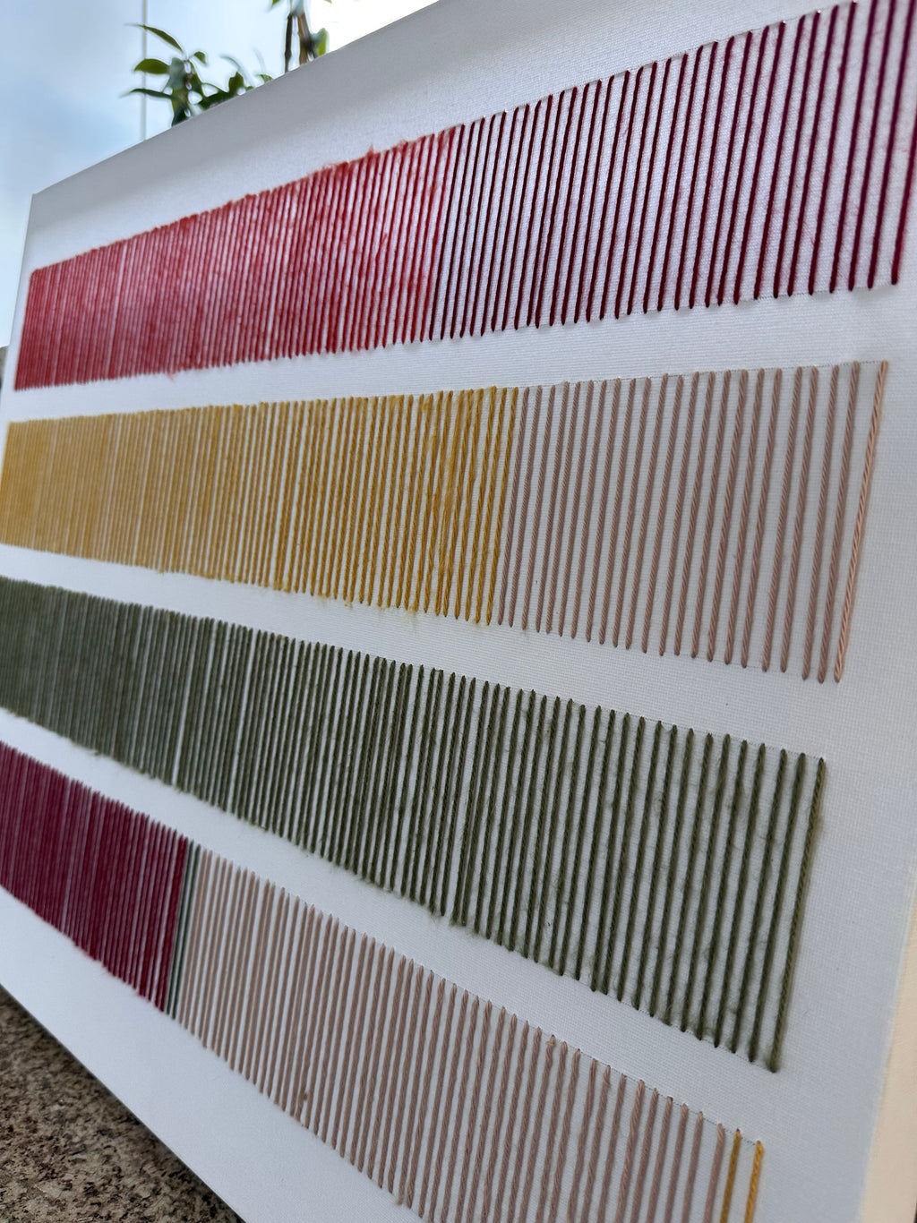 Cadence photographed at an angle, showing the raised texture of its hand-embroidered wool stitches in red, mustard, olive green and blush
