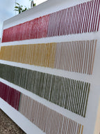 Cadence photographed at an angle, showing the raised texture of its hand-embroidered wool stitches in red, mustard, olive green and blush