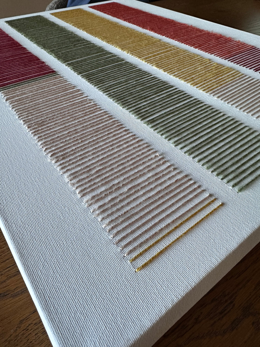 Angled close-up of Cadence's hand-embroidered wool stitches in blush, olive green, mustard and red on white canvas