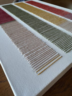Angled close-up of Cadence's hand-embroidered wool stitches in blush, olive green, mustard and red on white canvas