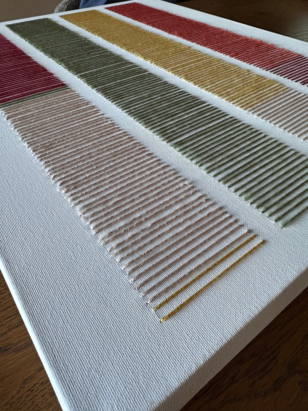 Angled close-up of Cadence's hand-embroidered wool stitches in blush, olive green, mustard and red on white canvas
