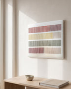 Cadence, hand-embroidered textile wall art by Nyra Atelier, hanging on a white plaster wall above a pale oak console with a stoneware bowl and a linen-bound book, in morning window light. AI-assisted lifestyle image: the setting is illustrative and the canvas is our real product photo; please refer to our real product photographs for the actual item’s details.