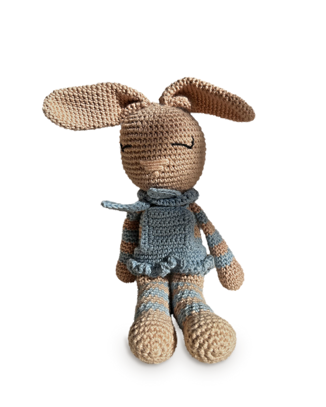 Celeste, a handmade crochet bunny by Nyra Atelier with long floppy tan ears, a sky blue ruffled dress with a tied neck bow and blue-and-beige striped arms and legs, seated