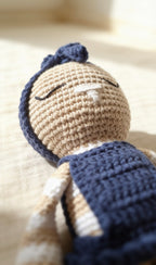 Mia, handmade crochet bunny, lying down in her navy blue crochet dress and bow headband