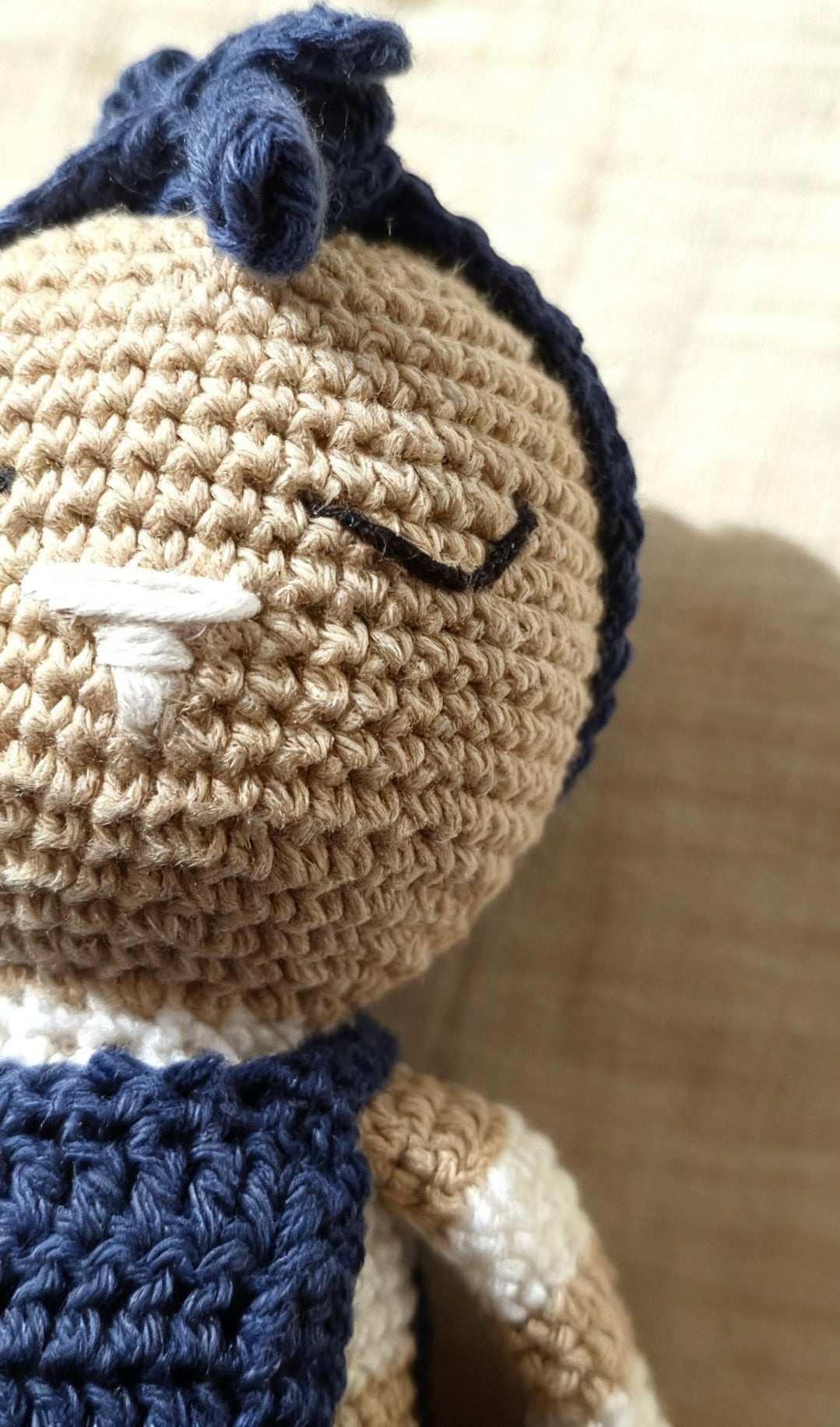 Close-up of Mia's crocheted face: embroidered sleeping eyes, a stitched nose and handmade cotton stitches