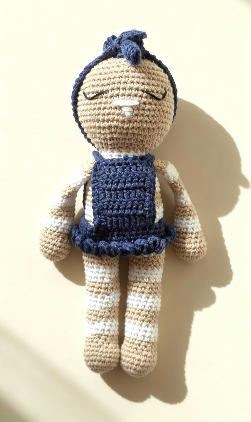 Mia, handmade crochet bunny in her navy blue dress and bow headband, standing against a warm cream background