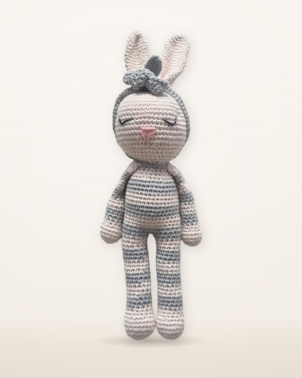 Luna, handmade crochet bunny by Nyra Atelier with grey and cream stripes, pale pink inner ears and a grey flower headband, studio photo on a warm ivory background