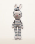 Luna, handmade crochet bunny by Nyra Atelier with grey and cream stripes, pale pink inner ears and a grey flower headband, studio photo on a warm ivory background