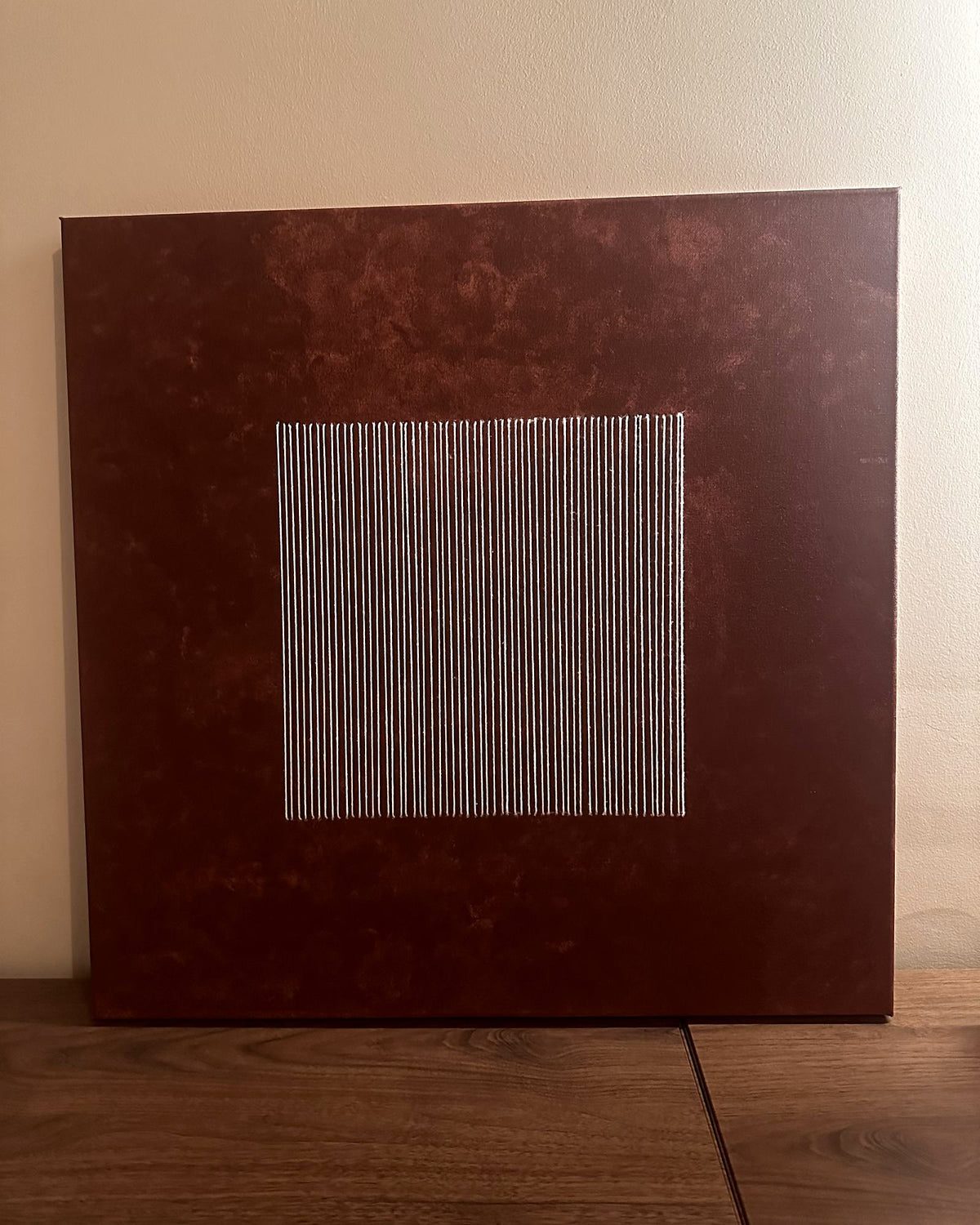 Legato von Nyra Atelier, Vorderansicht: von Hand in Erdrot bemalte Leinwand mit einem Quadrat aus handgestickten elfenbeinfarbenen Fadenlinien