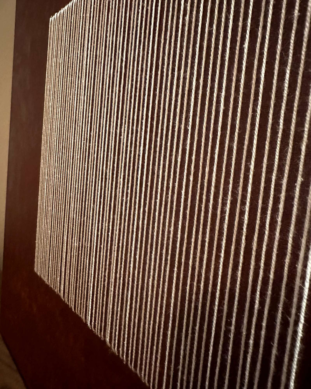 Nahaufnahme von Legato im Streiflicht: senkrechte elfenbeinfarbene Fäden über der strukturierten erdroten Farbe