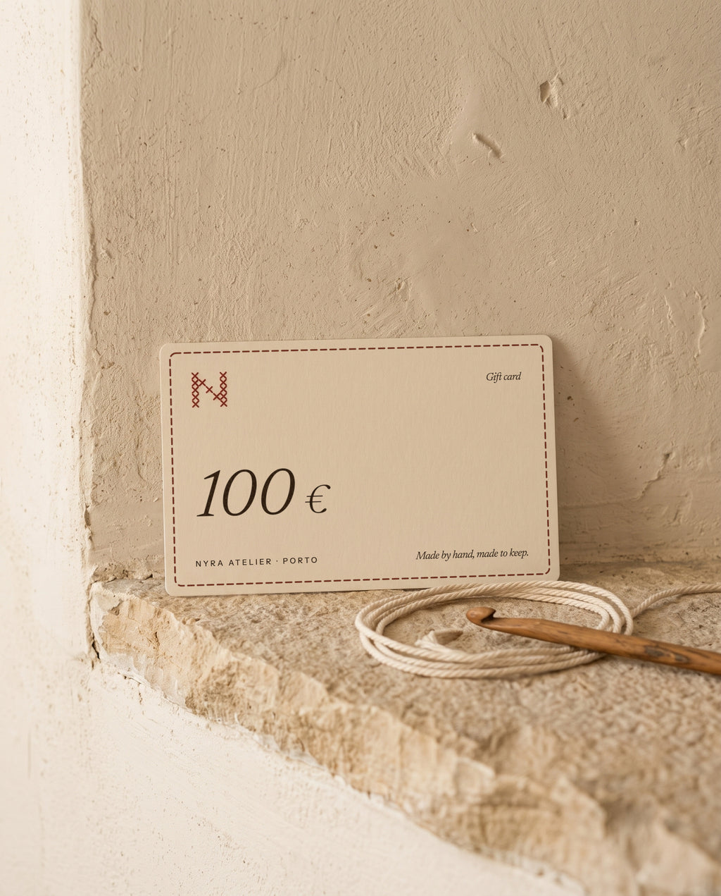 Nyra Atelier gift card for 100 €, on a limestone ledge with cotton cord and a crochet hook (AI setting)