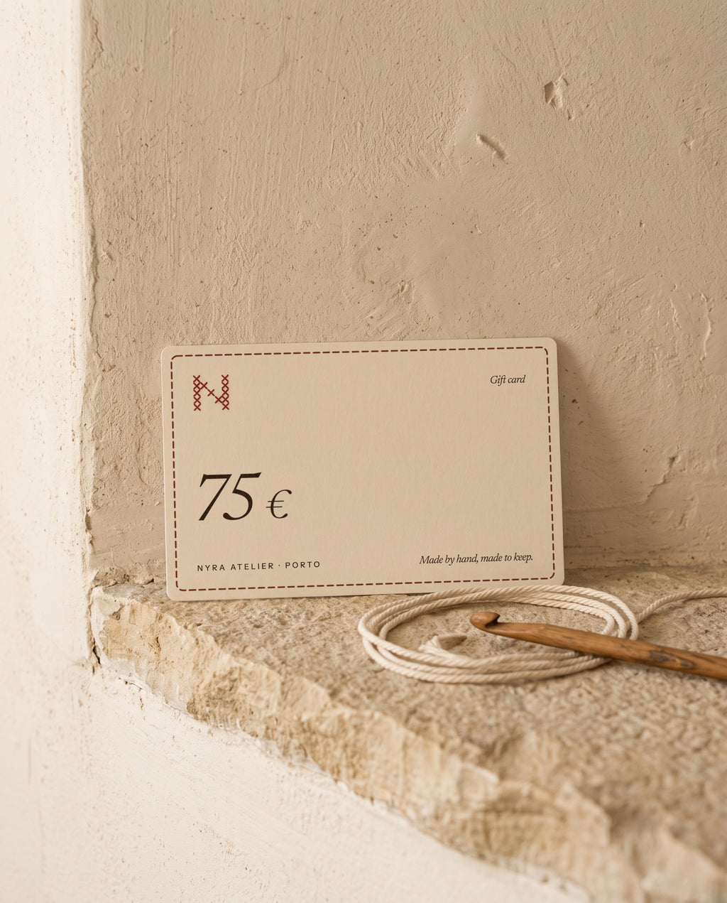 Nyra Atelier gift card for 75 €, on a limestone ledge with cotton cord and a crochet hook (AI setting)