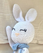 Close-up of Theo's crocheted face, with embroidered sleepy eyes, a stitched peach nose, long ears and a light blue neck bow, made by hand in Porto