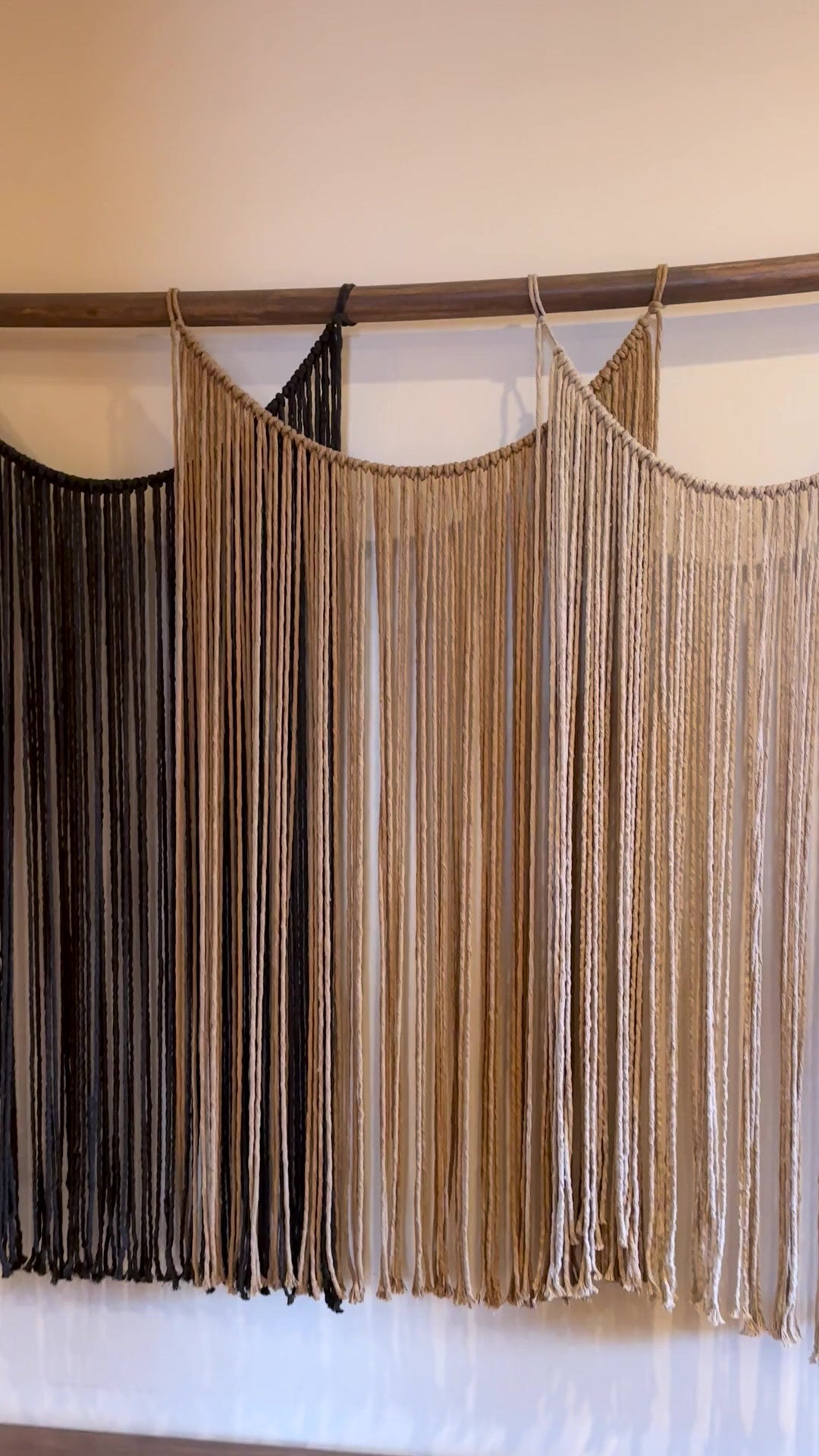 Suspenso Terra, large handmade macramé wall hanging in charcoal, caramel and taupe by Nyra Atelier, on a warm plaster wall in the Porto atelier