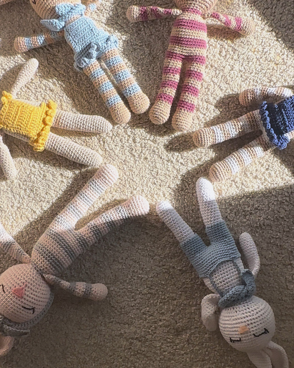 The Nyra Bunny Family, six handmade crochet bunnies by Nyra Atelier, lying in a star on a sunlit rug, then one by one on the sofa, and Sónia's hands dressing Sol in her yellow dress