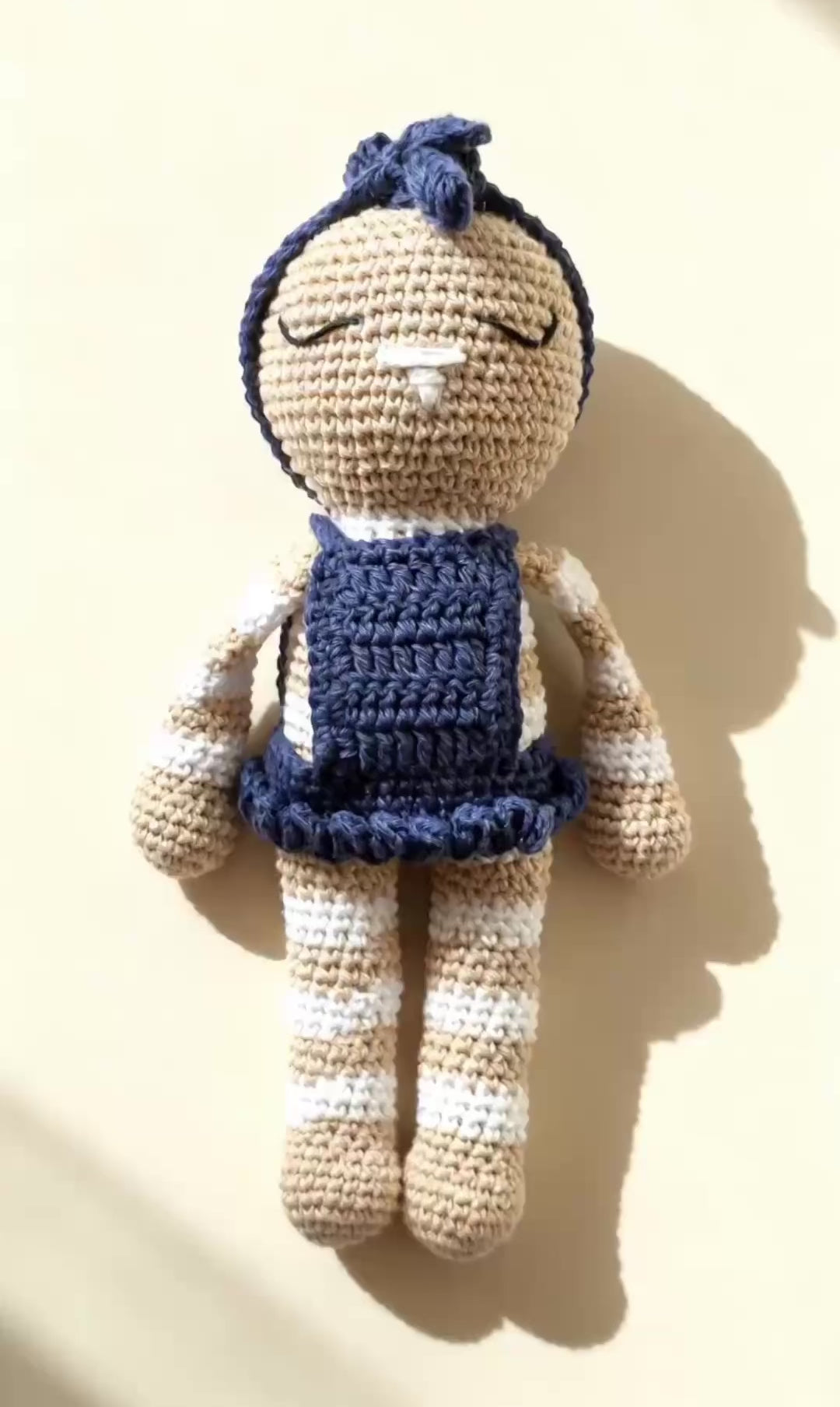 Video: Mia, handmade crochet bunny in her navy blue dress, standing against a cream background, with a slow zoom to her face