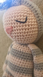 Close-up of Luna's crocheted face: embroidered sleeping eyes, a pink nose and the grey flower headband