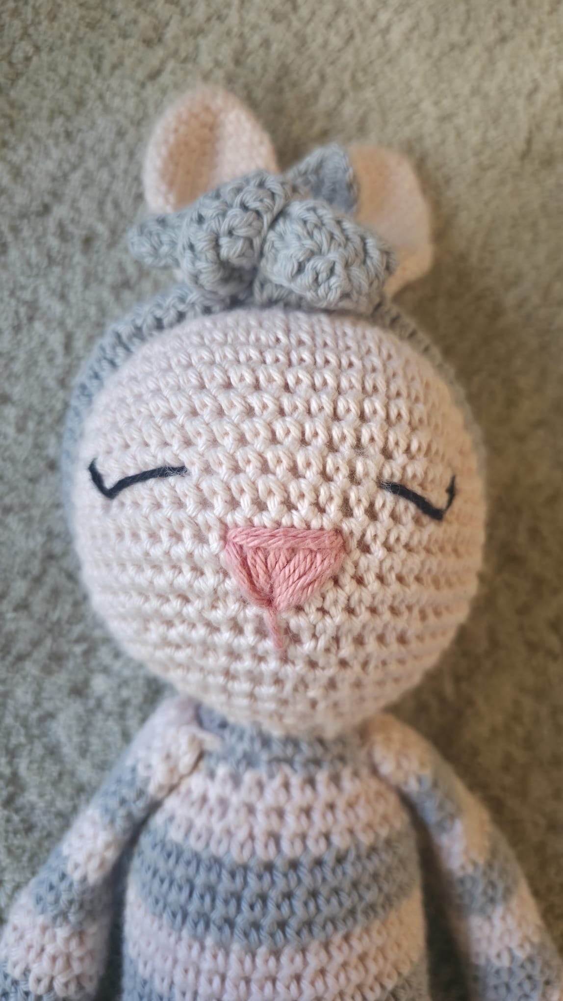 Luna, handmade crochet bunny with grey and cream stripes, a grey flower headband and a pink nose, close-up