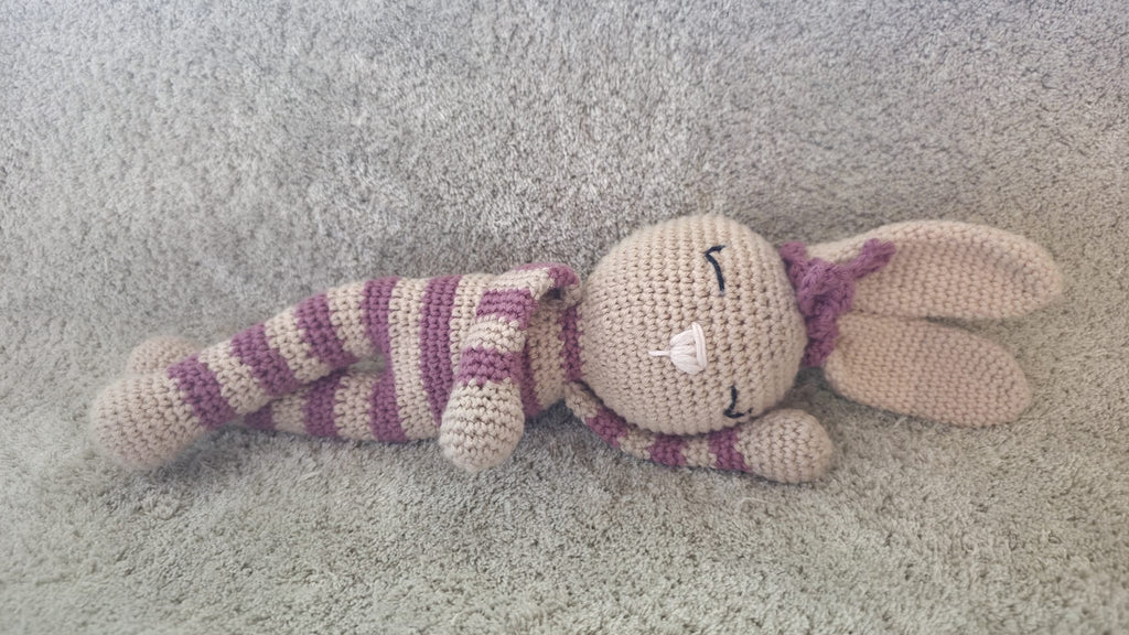 Rosa, handmade crochet bunny with pink and beige stripes, lying down