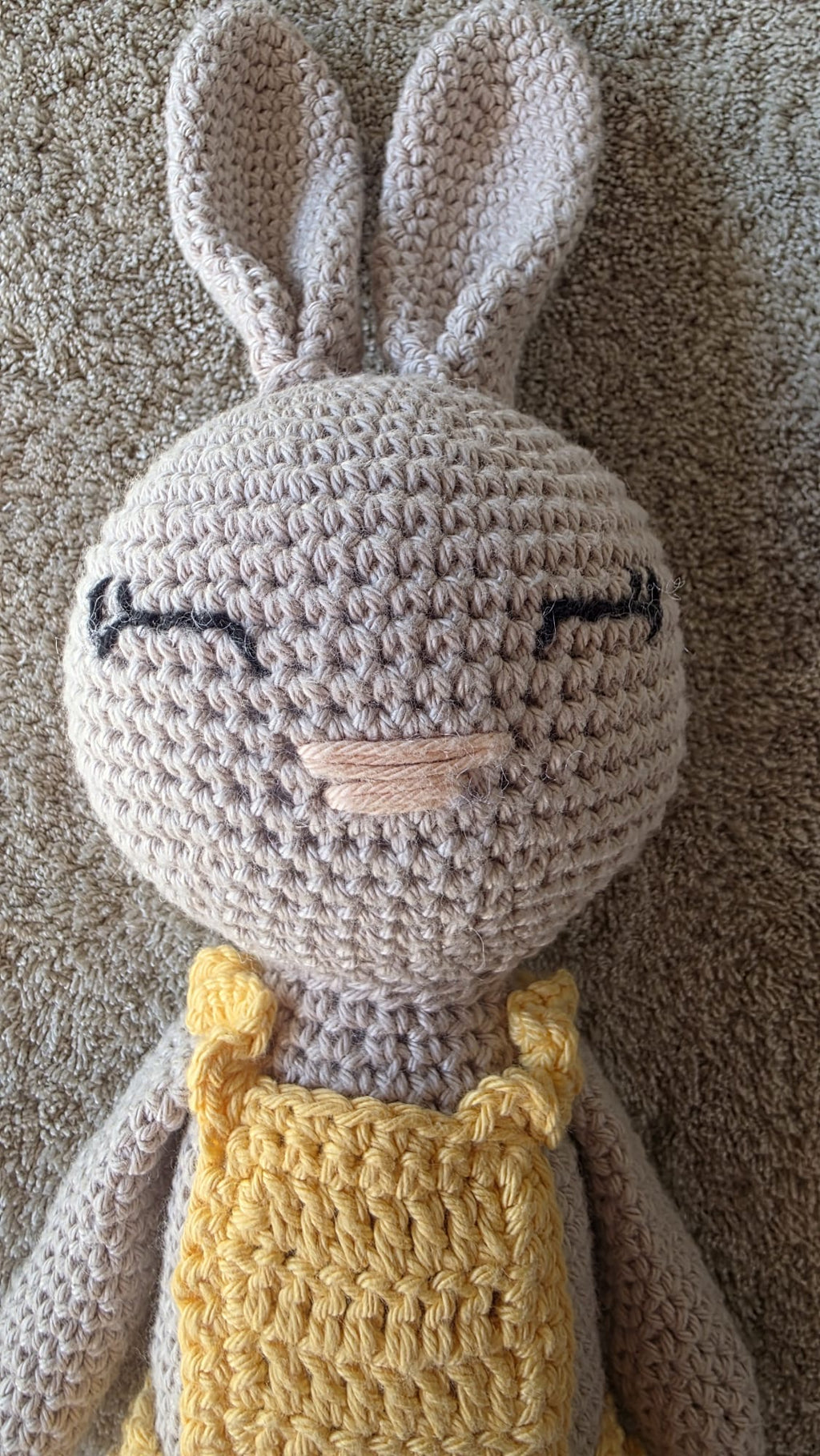 Close-up of Sol, handmade crochet bunny with a pale grey head, long ears and sleeping eyes, in her yellow crochet dress