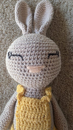 Close-up of Sol, handmade crochet bunny with a pale grey head, long ears and sleeping eyes, in her yellow crochet dress