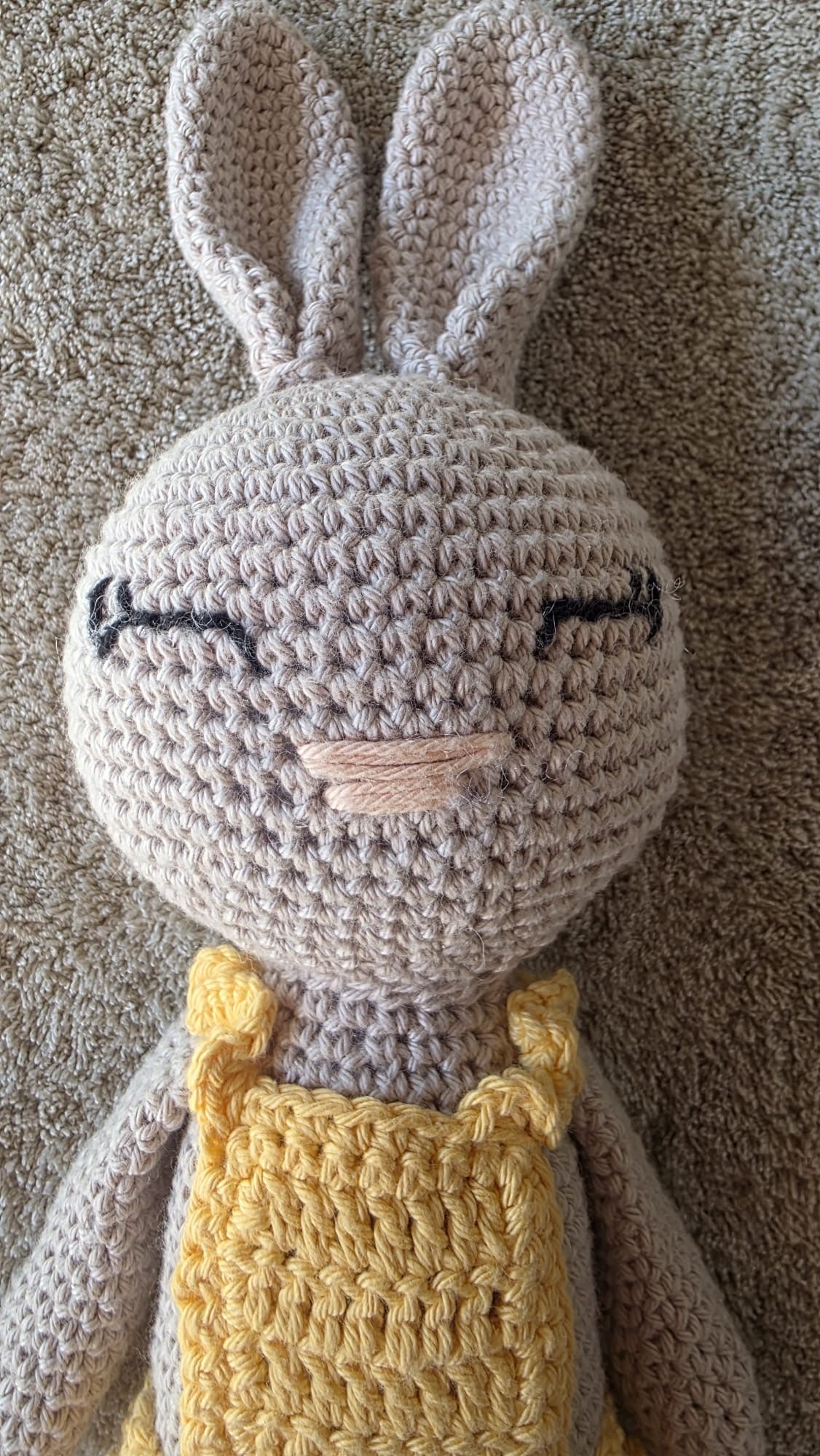 Close-up of Sol, handmade crochet bunny with a pale grey head, long ears and sleeping eyes, in her yellow crochet dress