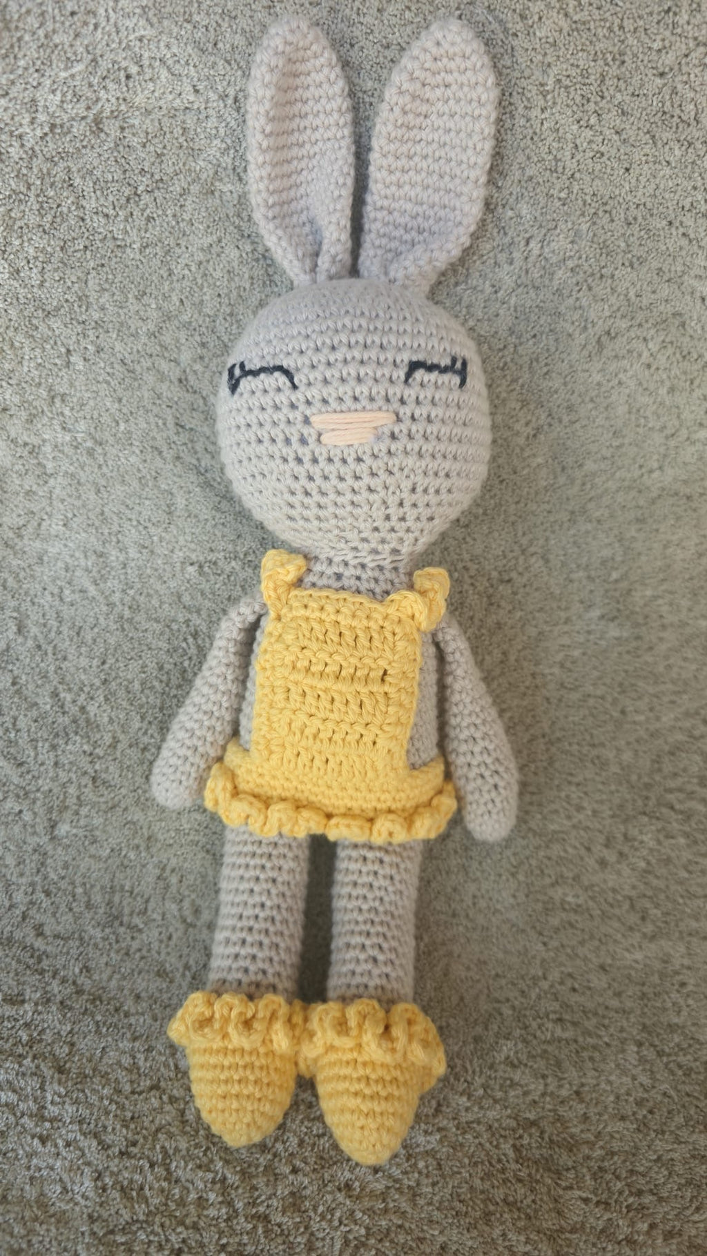 Sol, handmade crochet bunny with a pale grey body and long ears, in her yellow ruffled dress and shoes, standing