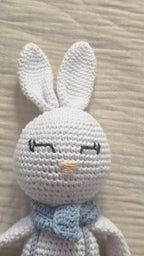 Close-up of Theo, handmade white crochet bunny with long ears, embroidered sleeping eyes and a light blue neck bow