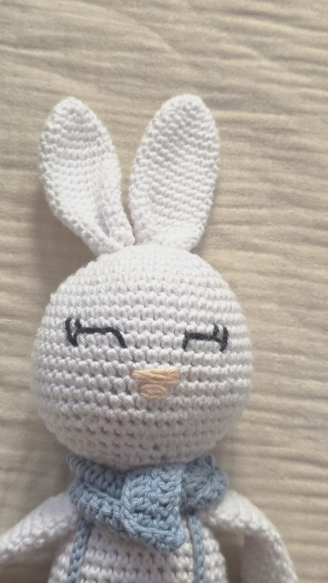 Close-up of Theo, handmade white crochet bunny with long ears, embroidered sleeping eyes and a light blue neck bow