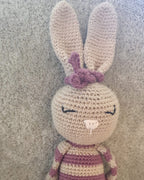 Close-up of Rosa, handmade crochet bunny: tan ears, a pink crochet bow, embroidered sleeping eyes and pink-and-beige stripes