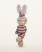 Rosa, handmade crochet bunny by Nyra Atelier with pink and beige stripes, tan ears and a pink bow, studio photo on a warm ivory background
