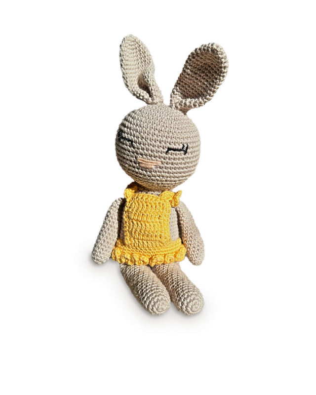 Sol, a handmade crochet bunny by Nyra Atelier with a pale greige body, tall ears and a sunny yellow ruffled dress, seated