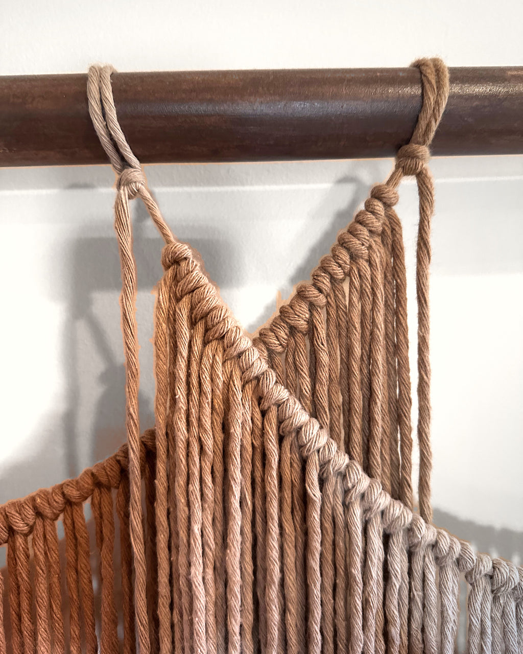 Close-up of Suspenso Terra: cords looped over the natural wooden branch where the caramel and taupe swags begin. Real photograph.