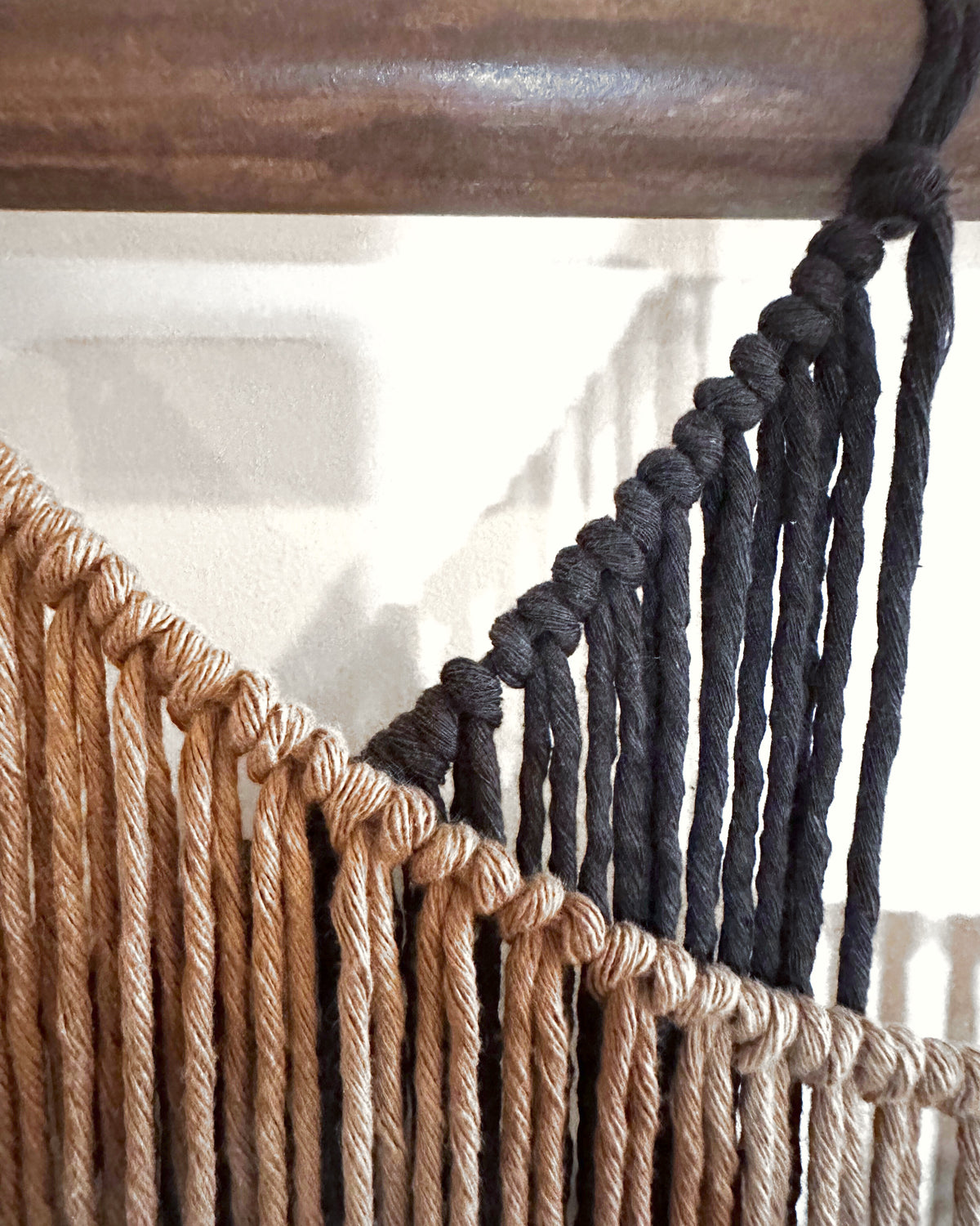Close-up of Suspenso Terra: the knotted swag of the caramel panel crossing the charcoal panel just below the wooden branch