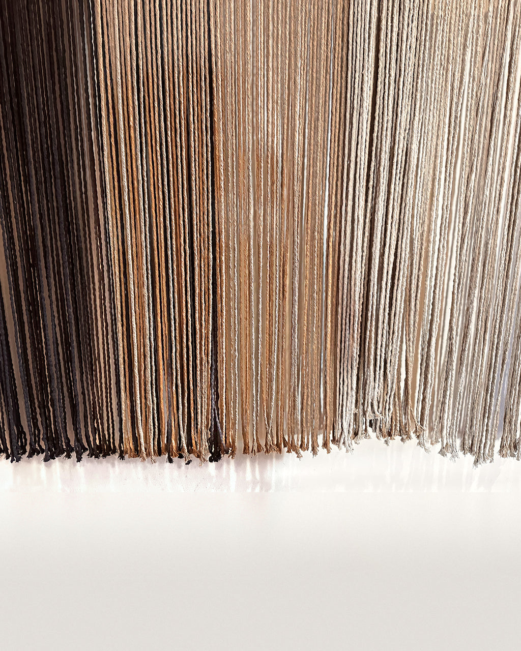 The long fringe of Suspenso Terra in its three tones, deep brown, caramel and soft taupe-grey. Real photograph.