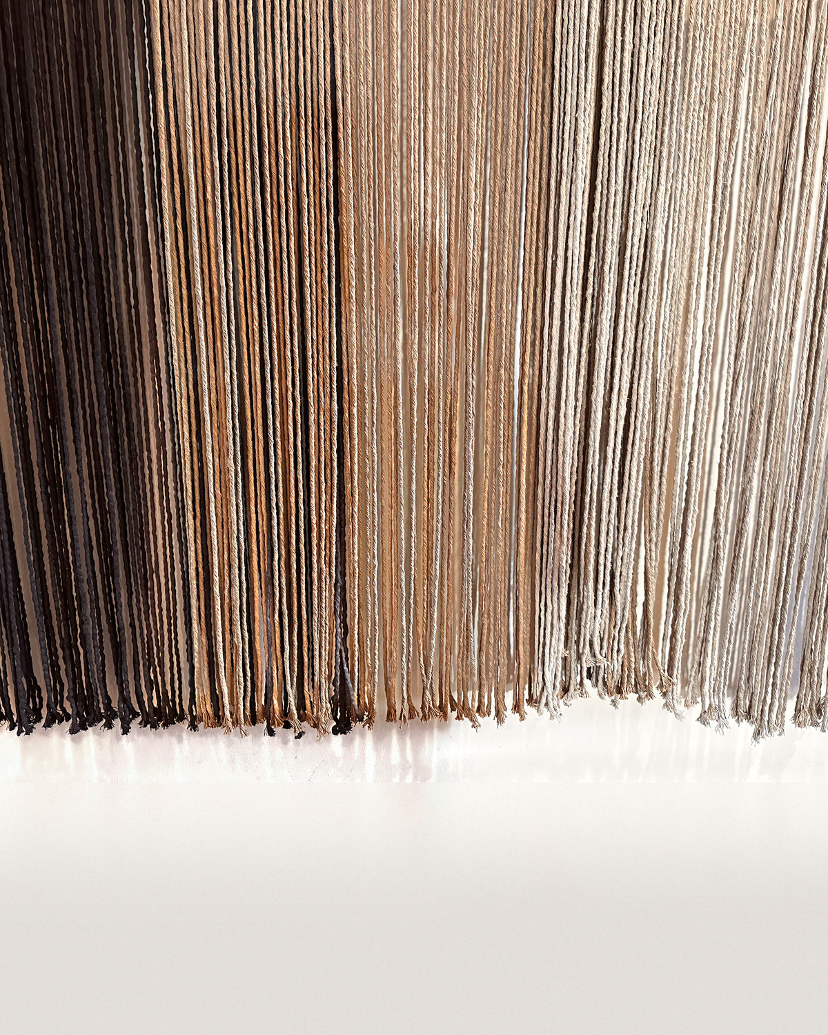 The long fringe of Suspenso Terra in its three tones, deep brown, caramel and soft taupe-grey. Real photograph.