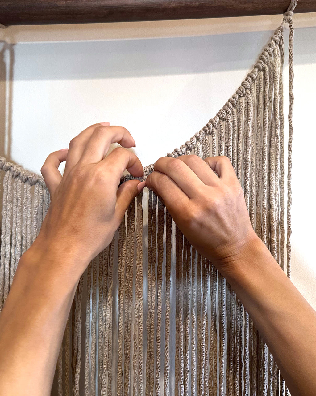 Sónia Bizarro's hands adjusting the knots along the top of a Suspenso Terra panel. Real photograph.