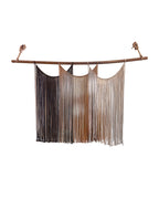Suspenso Terra, large handmade macramé wall hanging by Nyra Atelier: three draped panels of deep brown, caramel and taupe cord on a natural wooden branch hung with knotted rope. Real photograph on a plain white wall.