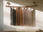 Suspenso Terra, large handmade macramé wall hanging by Nyra Atelier, on a lime-plaster wall above a limestone bench in afternoon sun. AI setting: the room was created with AI and the piece is real.