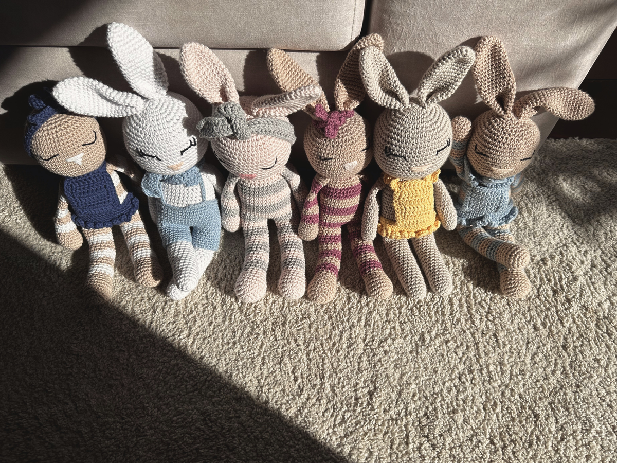 The Nyra Bunny Family: Mia, Theo, Luna, Rosa, Sol and Celeste, six handmade crochet bunnies by Nyra Atelier, sitting together in the afternoon sun.