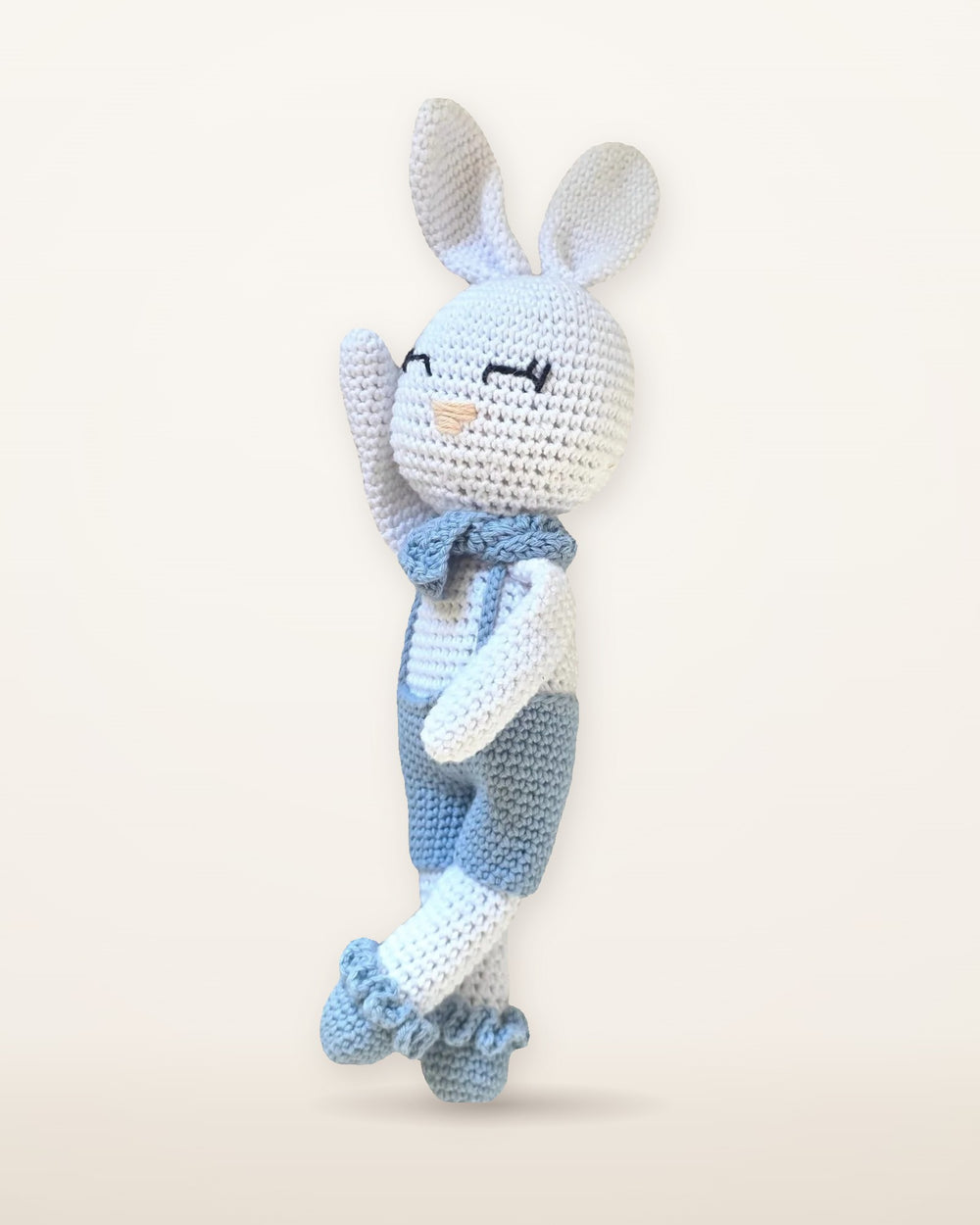 Theo, handmade white crochet bunny by Nyra Atelier with long ears, light blue overalls, neck bow and ruffled socks, studio photo on a warm ivory background
