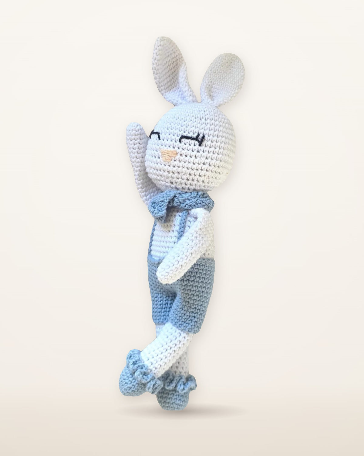 Theo, handmade white crochet bunny by Nyra Atelier with long ears, light blue overalls, neck bow and ruffled socks, studio photo on a warm ivory background
